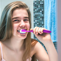 A youg girl brushing her teeth in the morning in front of her bath mirror, she has clean white teeth and a good attractive face